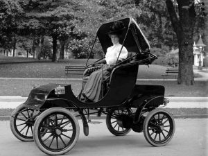 İlk elektrikli araba özelliği olan arabalardan birini sürmekte olan bir hanımefendiye ait görsel.